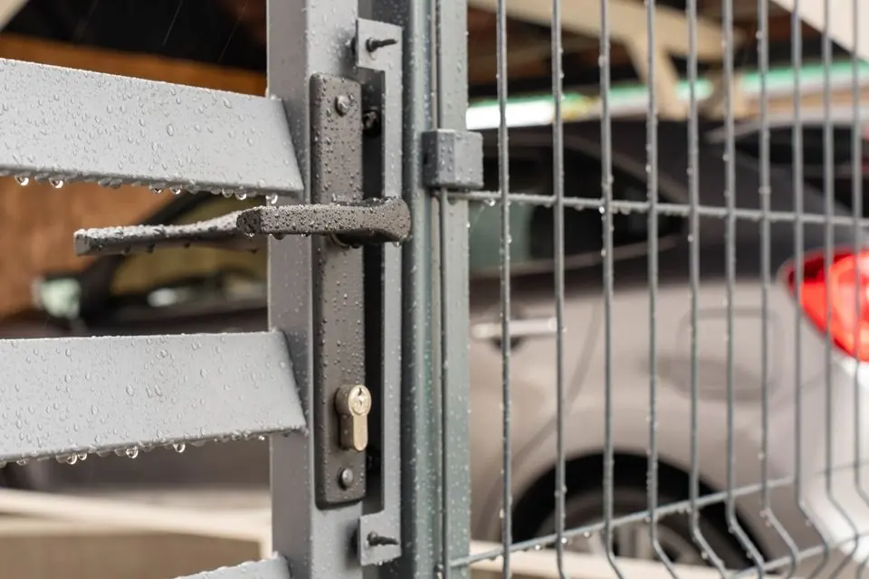 Close-Up of Wet Metal Gate with Car in Background