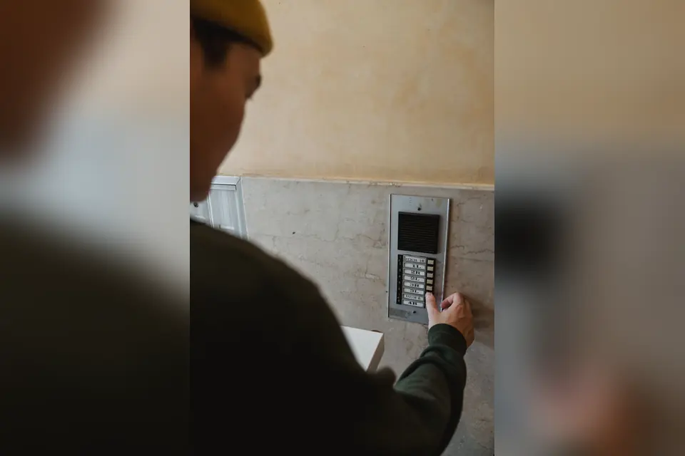 Man in Black Long Sleeve Shirt Pressing a Button on Intercom